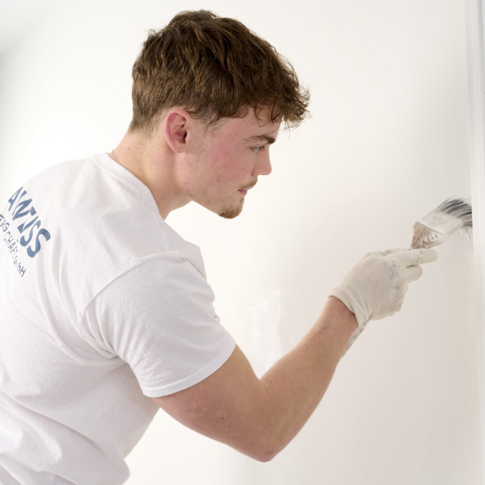 Marco Weiss von der DAWEISS Malergeschäft GmbH streicht eine helle Innenwand mit einem Pinsel.